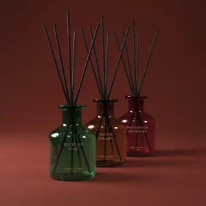 Mikados de Navidad Cerería Mollá en frascos verde, ámbar y rojo sobre fondo granate